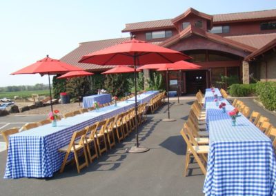 Outdoor tables and red market umbrellas set up for a harvest client lunch at Rack & Riddle's Alexander Valley location.