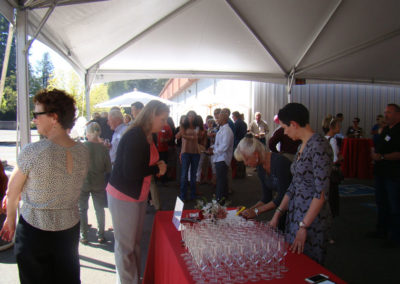Business Development Client Services Specialist standing at a table full of sparkling wine glasses, checking in guests with another employee at our Grand Opening event in 2014.