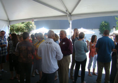 Party guests talking to each other under a tent. Some are holding glasses of sparkling wine.