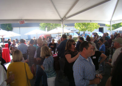 Lots of party guests during our Grand Opening Celebration in 2014, talking in groups and holding glasses of sparkling wine under a tent.