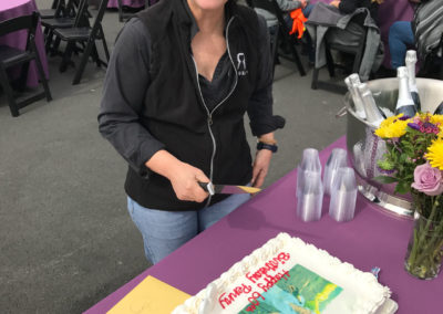 Penny Gadd-Coster cutting her birthday sheet cake with a big smile on her face.