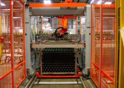 Front view of a steel tirage bin inside the automated transfer robot equipment, with many bottles stacked inside the bin cage.