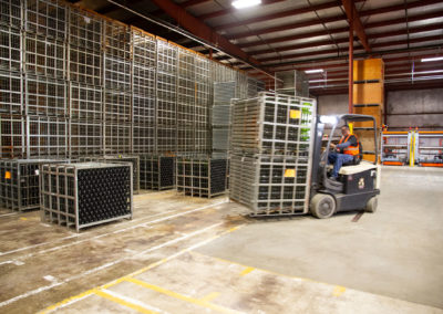 Forklift driver placing steel tirage bins filled with sparkling wine bottles into storage in the warehouse.