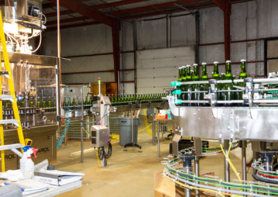 Side-angle view of the tirage bottling production line with many bottles rapidly traveling down conveyer.