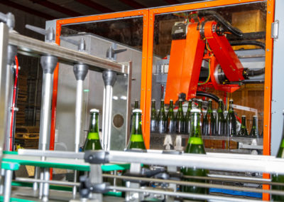 Sparkling wine bottles on tirage bottling production line being removed from conveyer by robot arm. Bottles are in the air after being lifted off the conveyer.