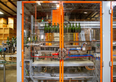 Bottle on tirage bottling production line being removed from conveyer by robotic arm. Bottles are in the air after being lifted off the conveyer.