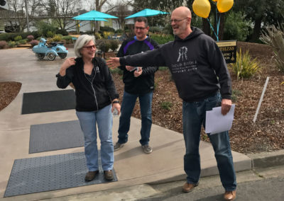 Bruce Lundquist & Mark Garaventa leading Penny Gadd-Coster along a sidewalk to enter her surprise 60th birthday party.