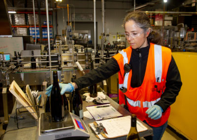 Production worker weighing wine bottles on scale for accuracy.